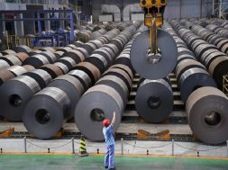 An employee guides a crane as it transports a roll of steel sheet, at a factory in Handan, Hebei