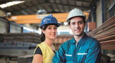 Pretty construction worker woman in factory looking smiling at camera